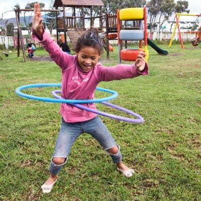 A volunteer with children in South Africa takes a picture of a young girl hula hooping outside a care centre in Cape Town. During a Childcare Project in South Africa, a young girl hula hoops outside a care centre.